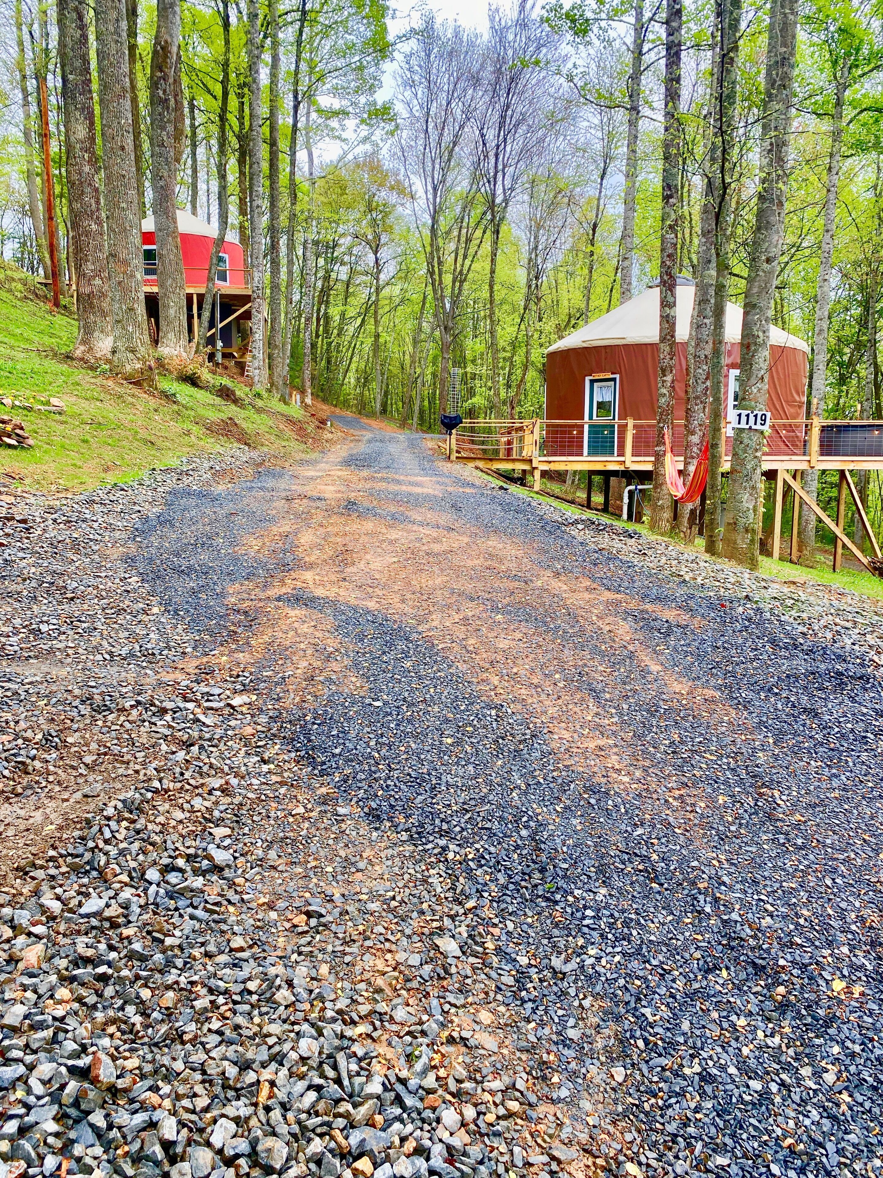 Un chemin de gravier mène à un chalet au toit rouge, entouré d’arbres.