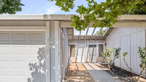 Un garage residenziale con facciata bianca, vialetto coperto e una piccola area giardino con alberi giovani.