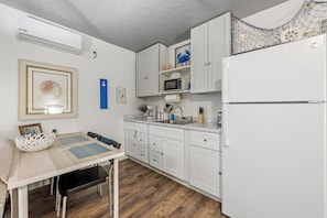 A compact kitchen with white cabinets, a microwave, a sink, and a refrigerator.