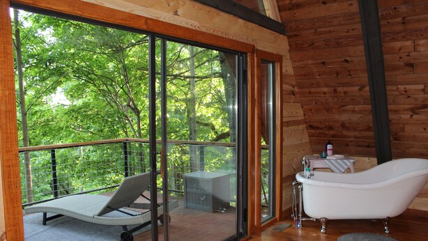 Eine Holzhütte mit einem verglasten Balkon, einer weißen Badewanne und einem kleinen Tisch mit einer Flasche.