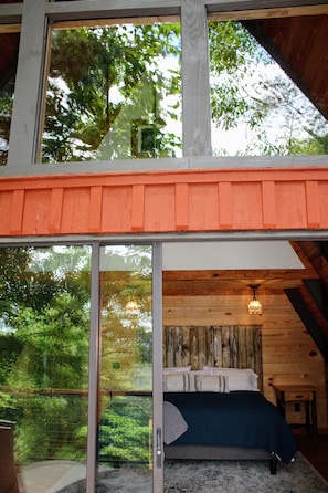 A bedroom with a large window, wooden ceiling, and a bed with pillows.