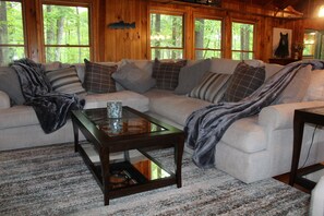 A cozy living room with a sectional sofa, a glass coffee table, and a view of the forest through large windows. - Private mountain cabin surrounded by Nat'l Forest! Visit wineries, hike the AT! (Cleveland)