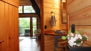 Ein Holzblockhaus-Innenraum mit einer hölzernen Bank, einem Waschbecken und einem Fenster mit Blick auf Grünflächen.