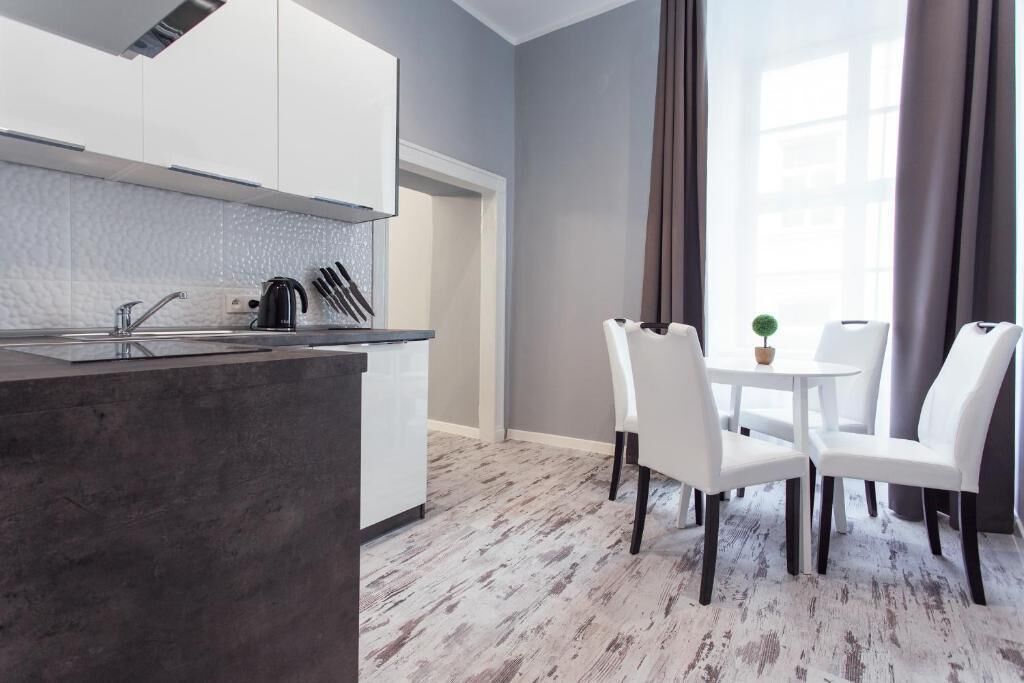 Eine moderne Küche mit weißen Schränken, einer zentralen Kücheninsel und einem Essbereich mit weißen Stühlen und einem kleinen Tisch.