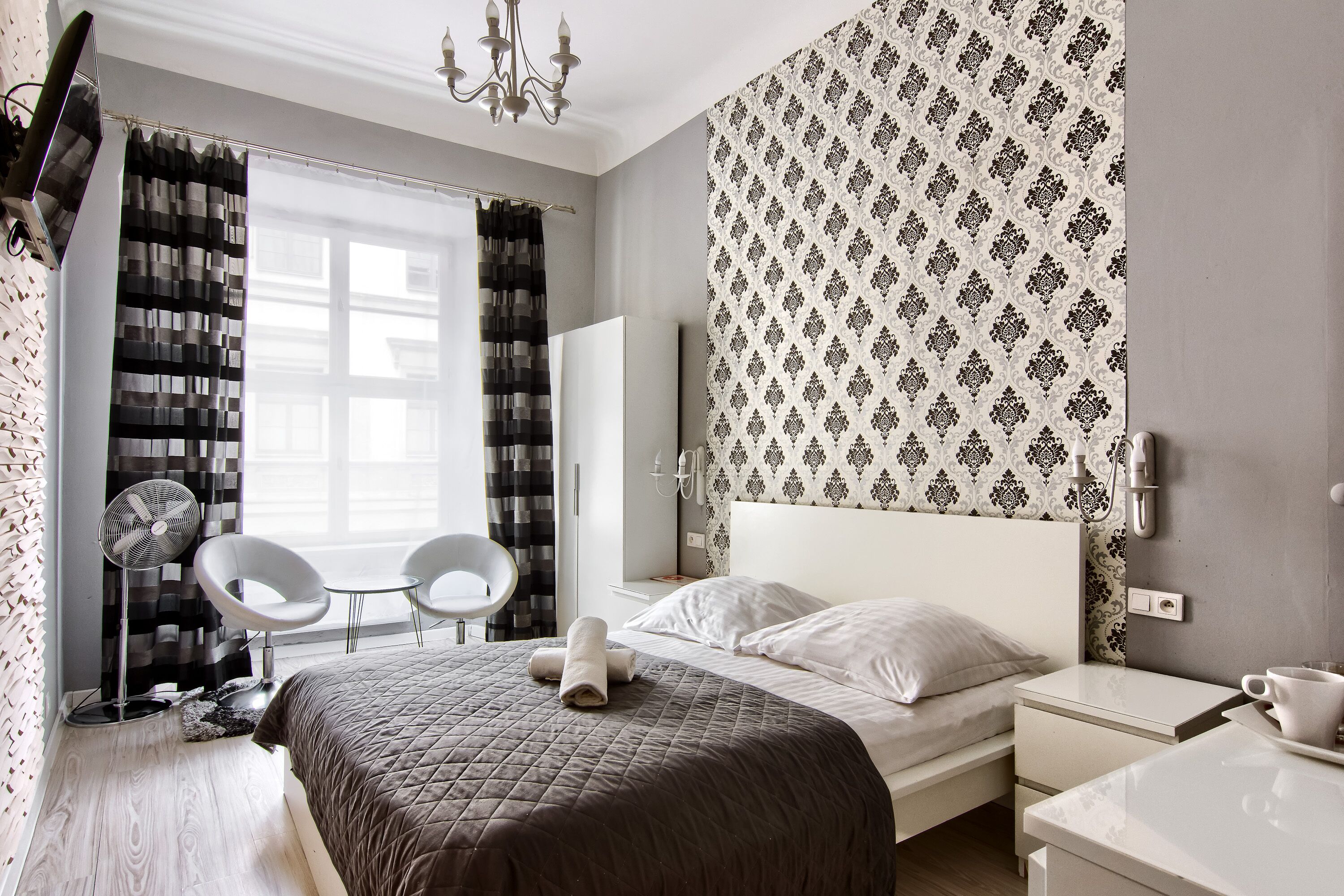 Une chambre d’hôtel moderne avec un grand lit, une table de chevet, une chaise, un bureau et une fenêtre avec des rideaux.