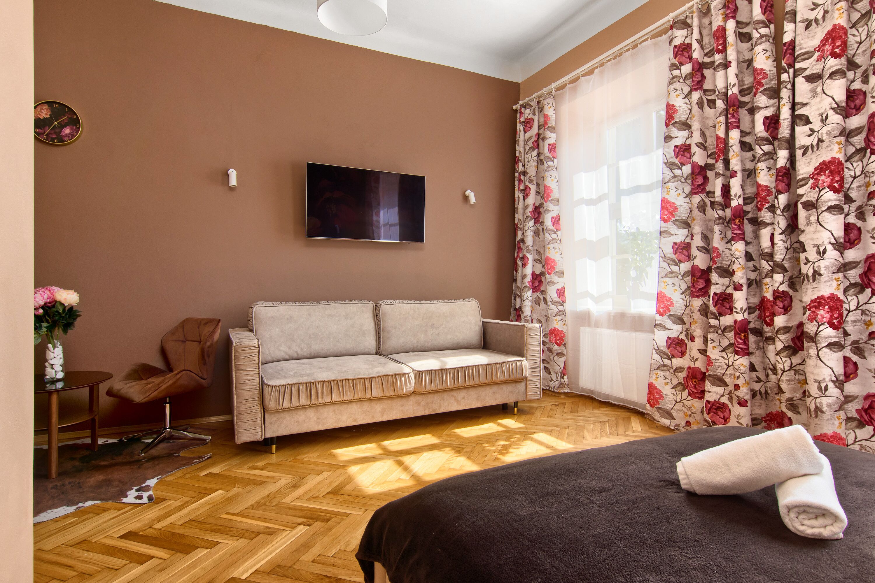 Una habitación con sofá, cama, televisor y ventana con cortinas florales.