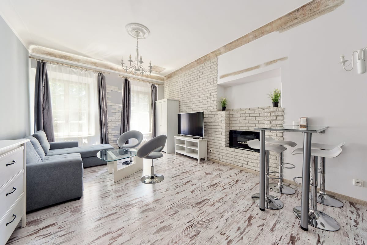 Ein modernes Wohnzimmer mit einem grauen Sofa, einem Glastisch, einem Fernseher und einem Kamin.