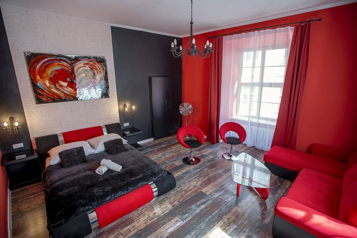 Ein modernes Hotelzimmer mit einem großen Bett, einem roten Sofa, einem Glastisch und einer roten und schwarzen Farbgestaltung.