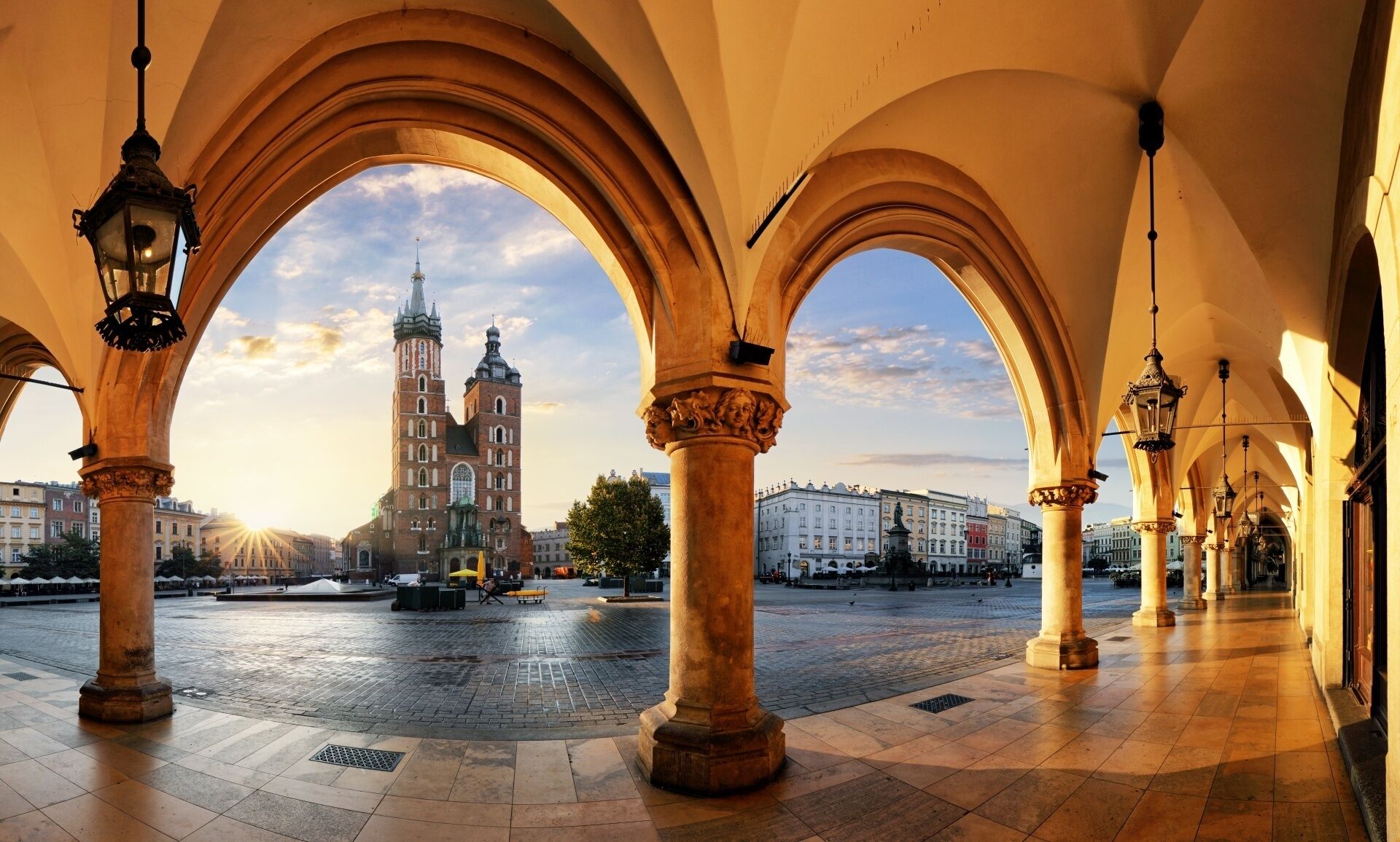 An open plaza with arches and columns, a prominent church with twin towers, and a clear sky.