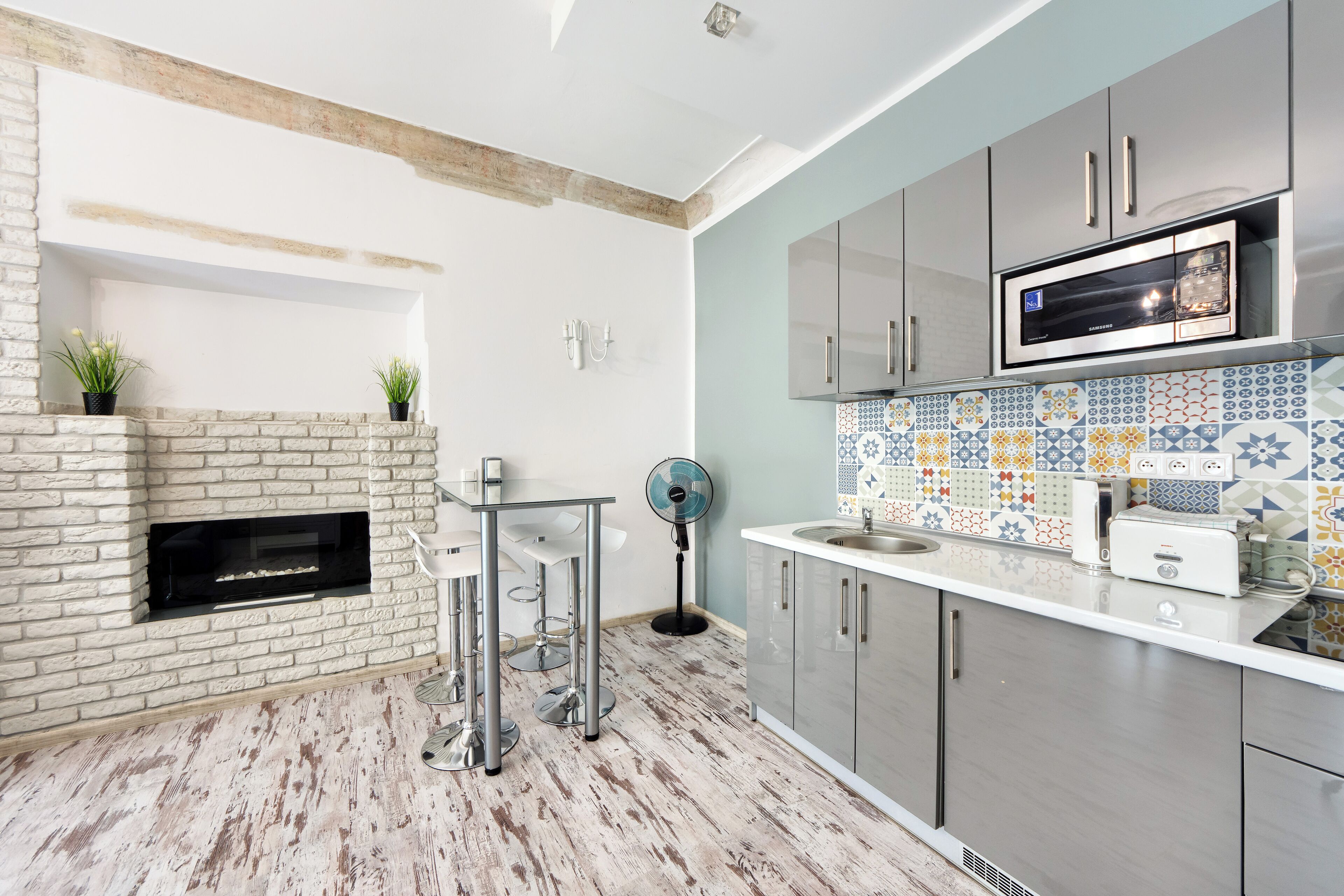Una cocina moderna con chimenea de ladrillo, electrodomésticos de acero inoxidable y un salpicadero de azulejos coloridos.