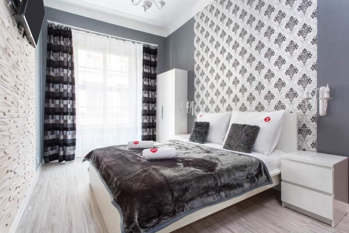 Ein modernes Schlafzimmer mit einem großen Bett, weißen Nachttischen, einem Kleiderschrank und gemusterten Vorhängen.