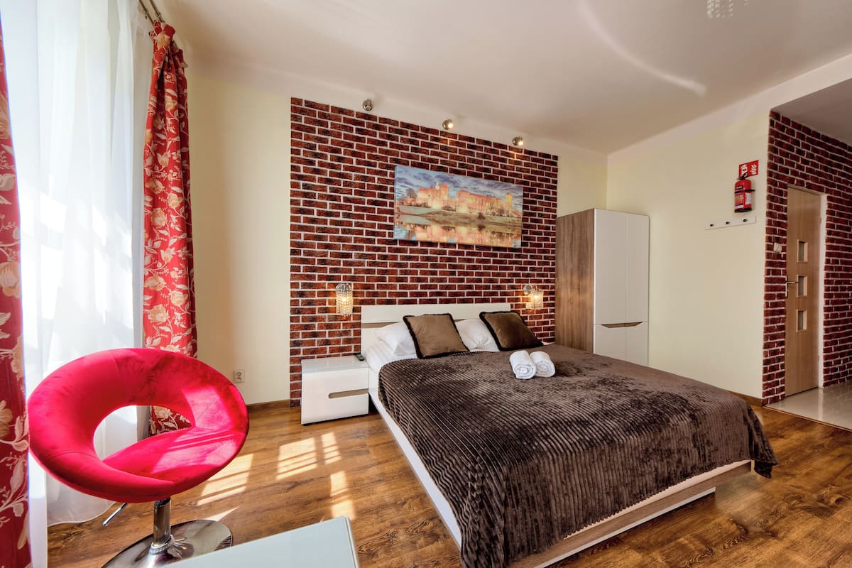Ein Schlafzimmer mit Backsteinwand, einem Bett mit brauner Decke, einem roten Stuhl und einem Stadtbild.