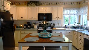 Una cocina con armarios blancos, un refrigerador negro, un microondas y una mesa de madera con individuales.