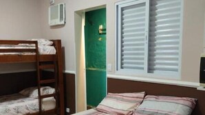Een slaapkamer met een stapelbed, een eenpersoonsbed, een raam met zonwering en een groene deur.
