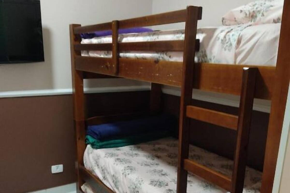 Une chambre avec des lits superposés, un téléviseur fixé au mur et un sol carrelé.