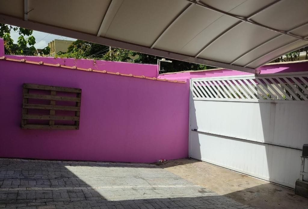 Um espaço ao ar livre coberto, com uma parede roxa, um portão branco e um palete de madeira.