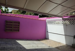 A covered outdoor area with a purple wall, a white gate, and a wooden pallet. - Hospedaria Antídoto (Guarujá)