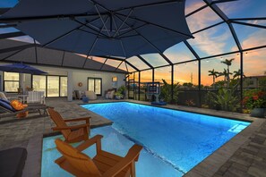 A swimming pool with a covered patio area, outdoor furniture, and a view of the sunset. - Sunshine Escape (Cape Coral)