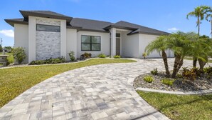 Una casa moderna a due piani con facciata in pietra, ampie finestre e un vialetto curvo che conduce all'ingresso.