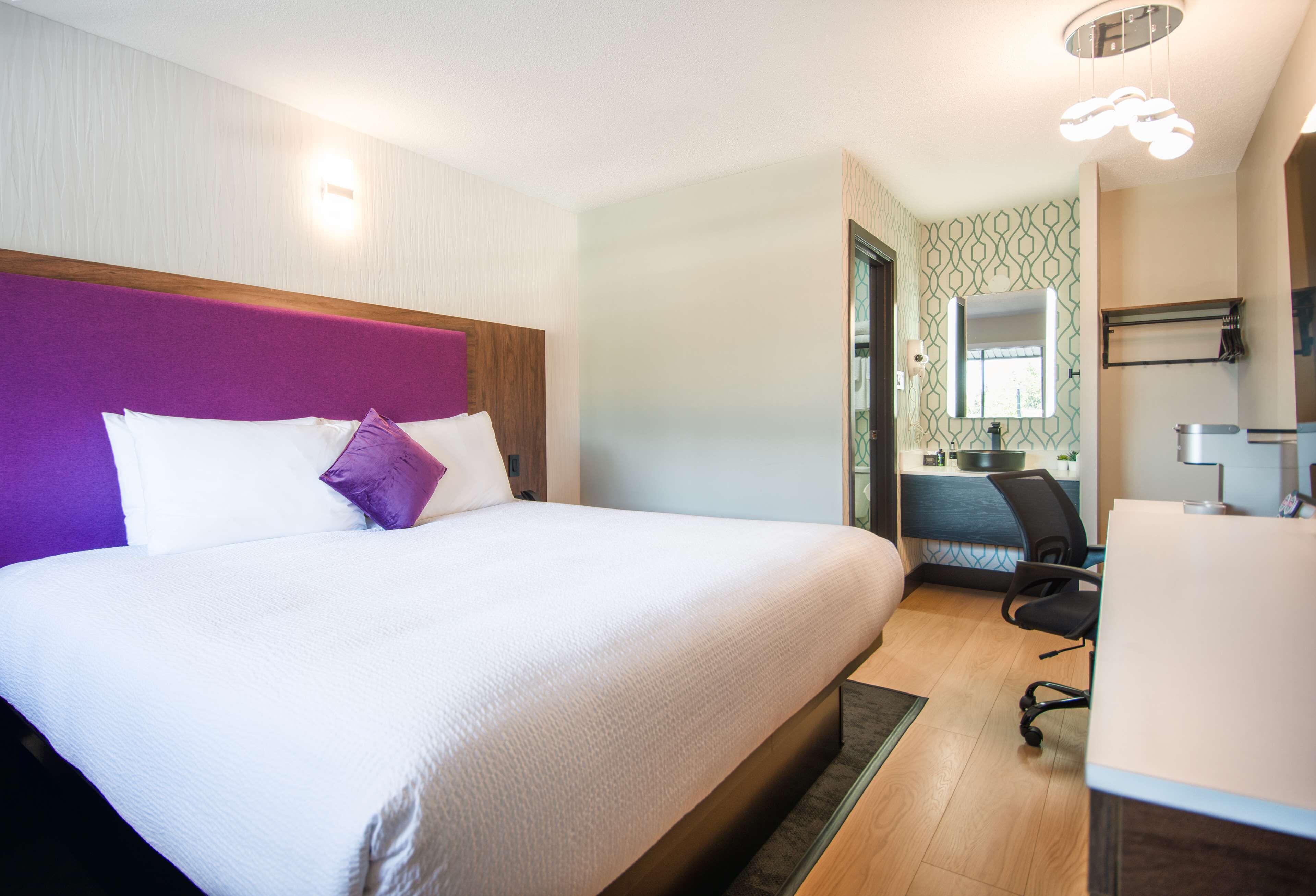 Una habitación de hotel moderna con una cama grande, un escritorio y un baño visible a través de una puerta abierta.