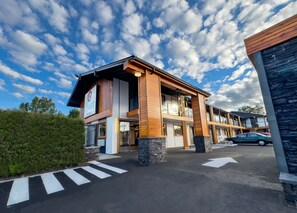 Un hotel moderno con un llamativo letrero de 'COAST Hotels', un área exterior cubierta y un estacionamiento con flechas direccionales.