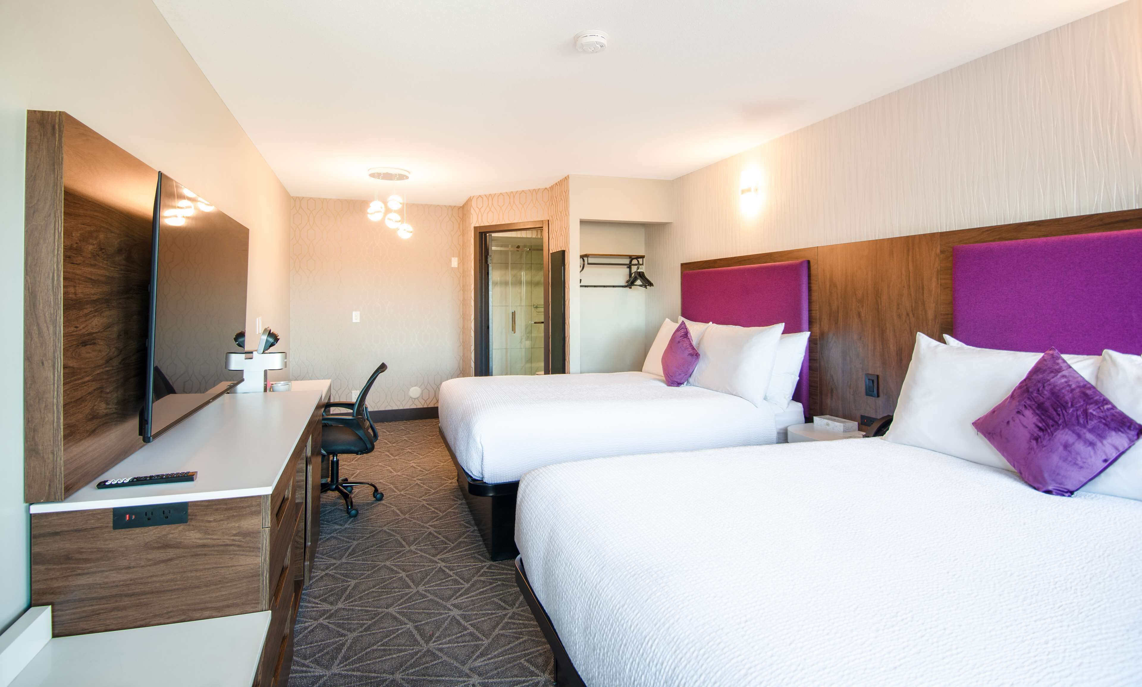 Habitación de hotel con dos camas, un escritorio, una silla, un espejo y zona de ducha.