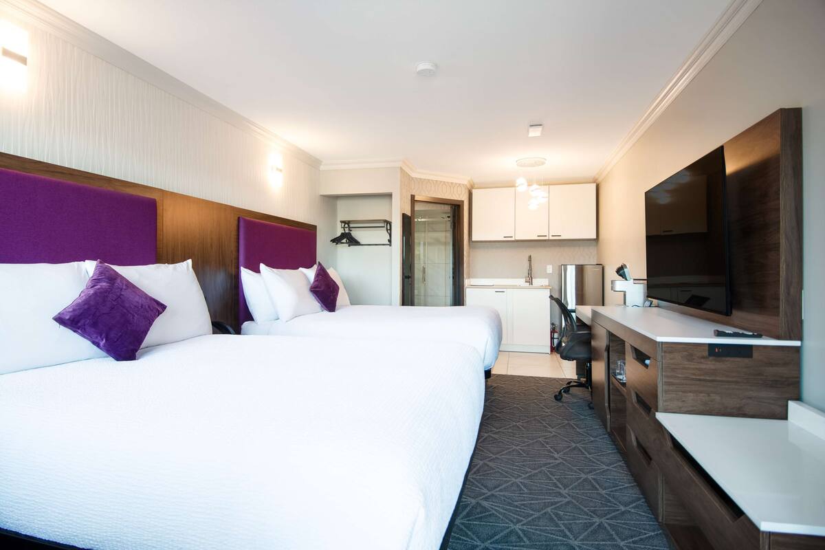A hotel room with a large bed, a desk, a television, and a kitchenette.