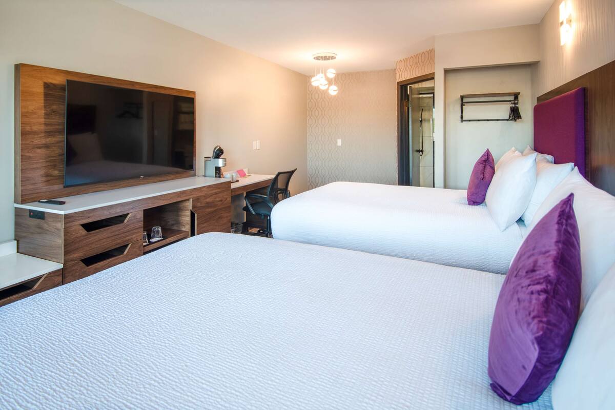 A hotel room with two beds, a TV, a desk, and a shower area.