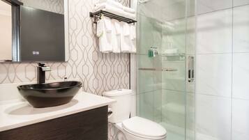 A modern bathroom with a black vessel sink, white toilet, and a glass-enclosed shower.