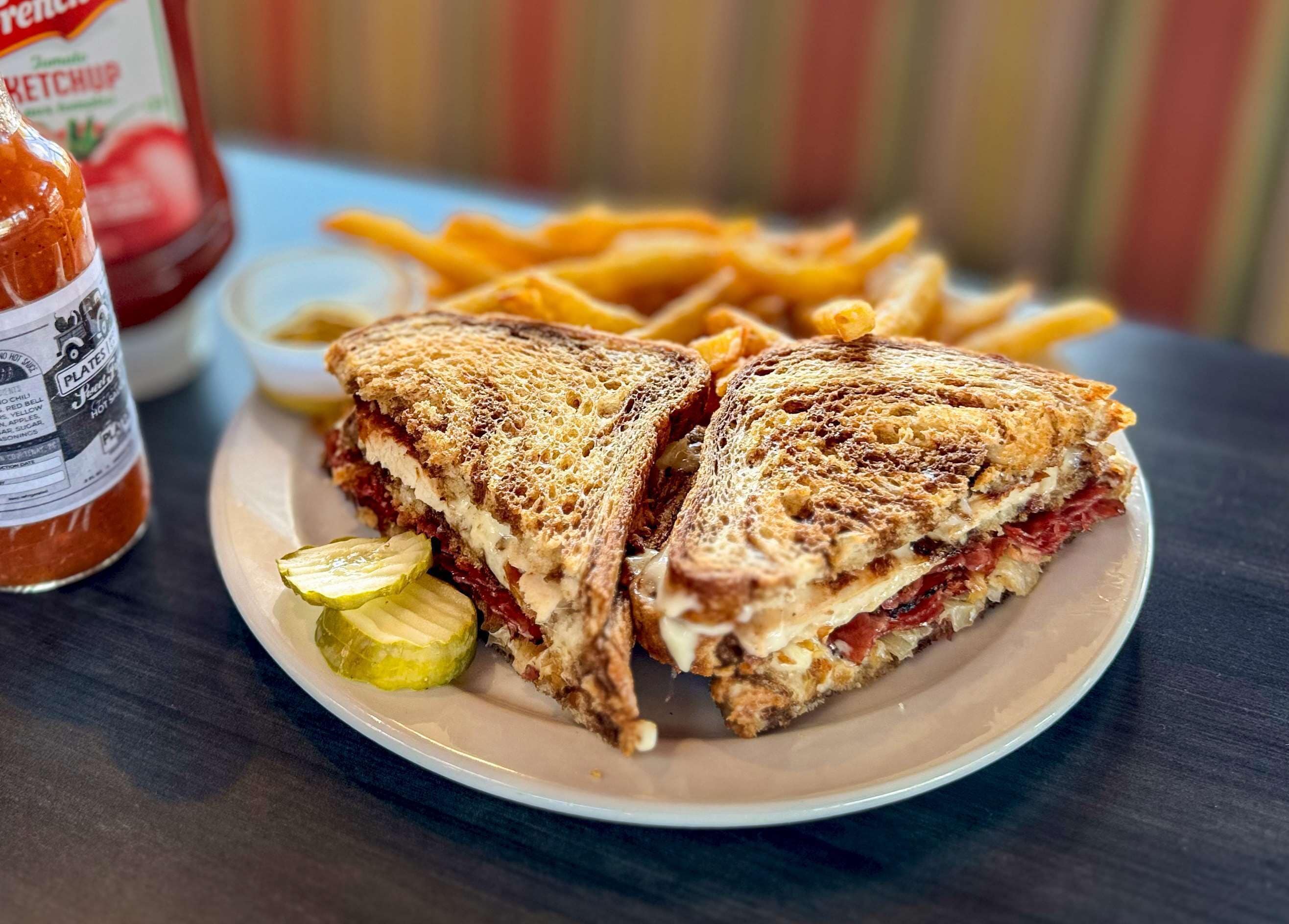 Un plato con un sándwich a la plancha, papas fritas y pepinillos.