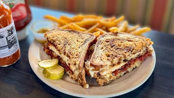 Un plato con un sándwich a la plancha, papas fritas y pepinillos.