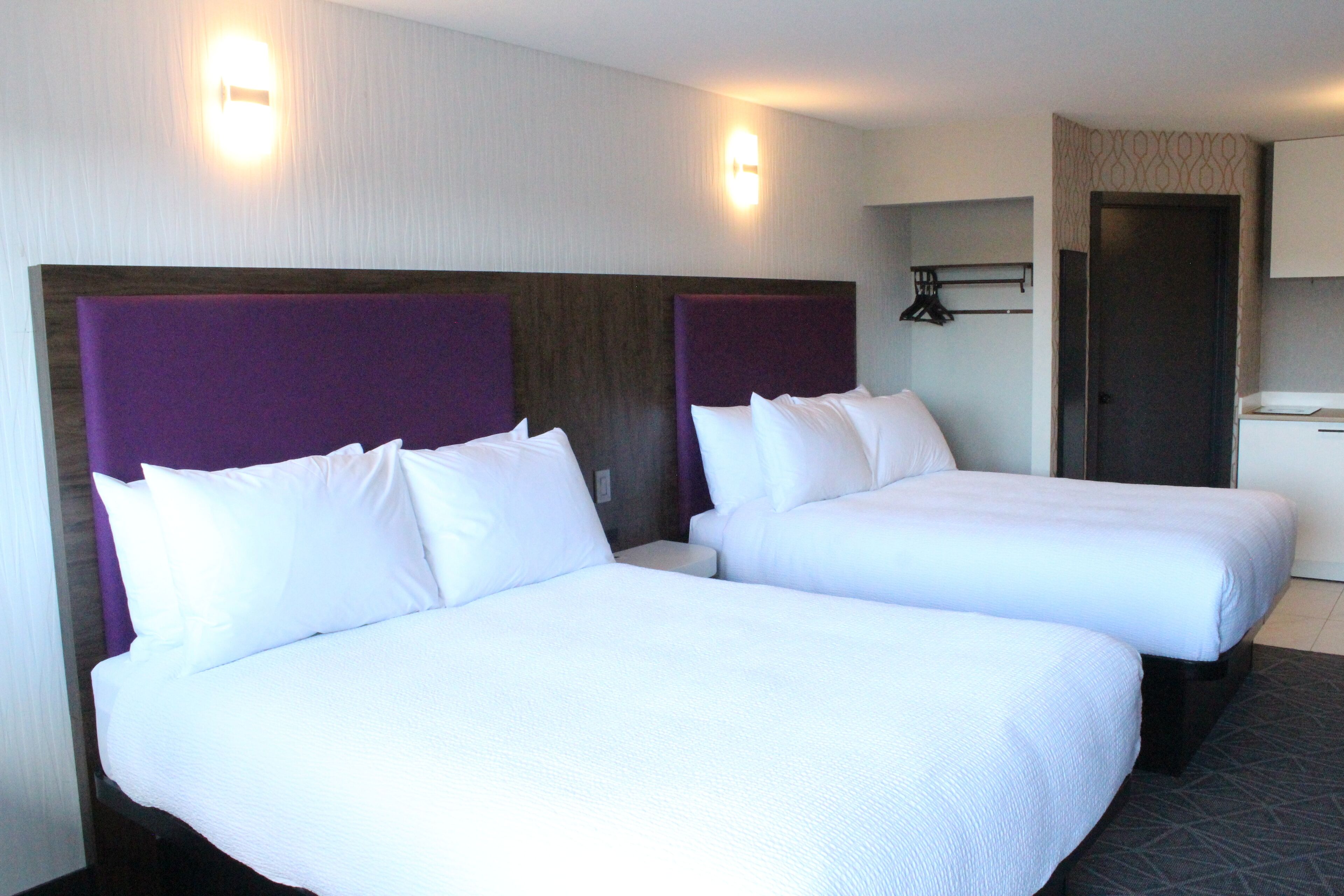 A hotel room with two beds, a wooden headboard, a small table, and a wardrobe.