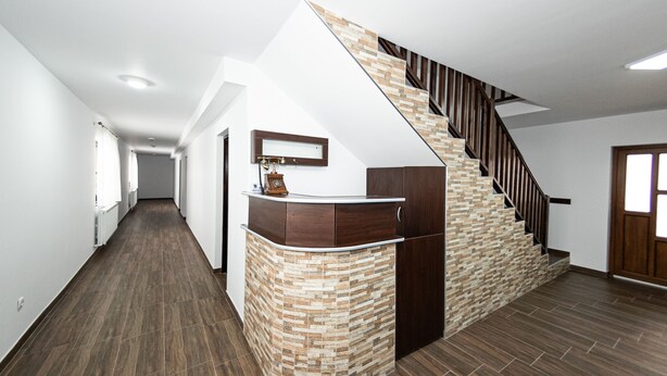 A modern interior with a curved reception desk, a staircase with a wooden finish, and a hallway with wooden flooring. - Casa Câmpulungeană (Campulung Moldovenesc)
