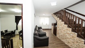A modern living area with a sofa, dining table, and chairs, a staircase with wooden railings, and a kitchen in the background. - Casa Câmpulungeană (Campulung Moldovenesc)