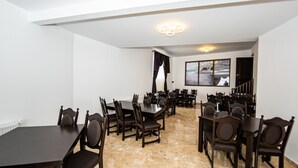 A dining area with multiple tables and chairs, a large window with a view, and a staircase leading to another floor. - Casa Câmpulungeană (Campulung Moldovenesc)