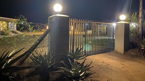 A gated entrance with two light poles, a chain-link fence, and some desert vegetation. - Wanakah Estate Guesthouse (Mpaka)