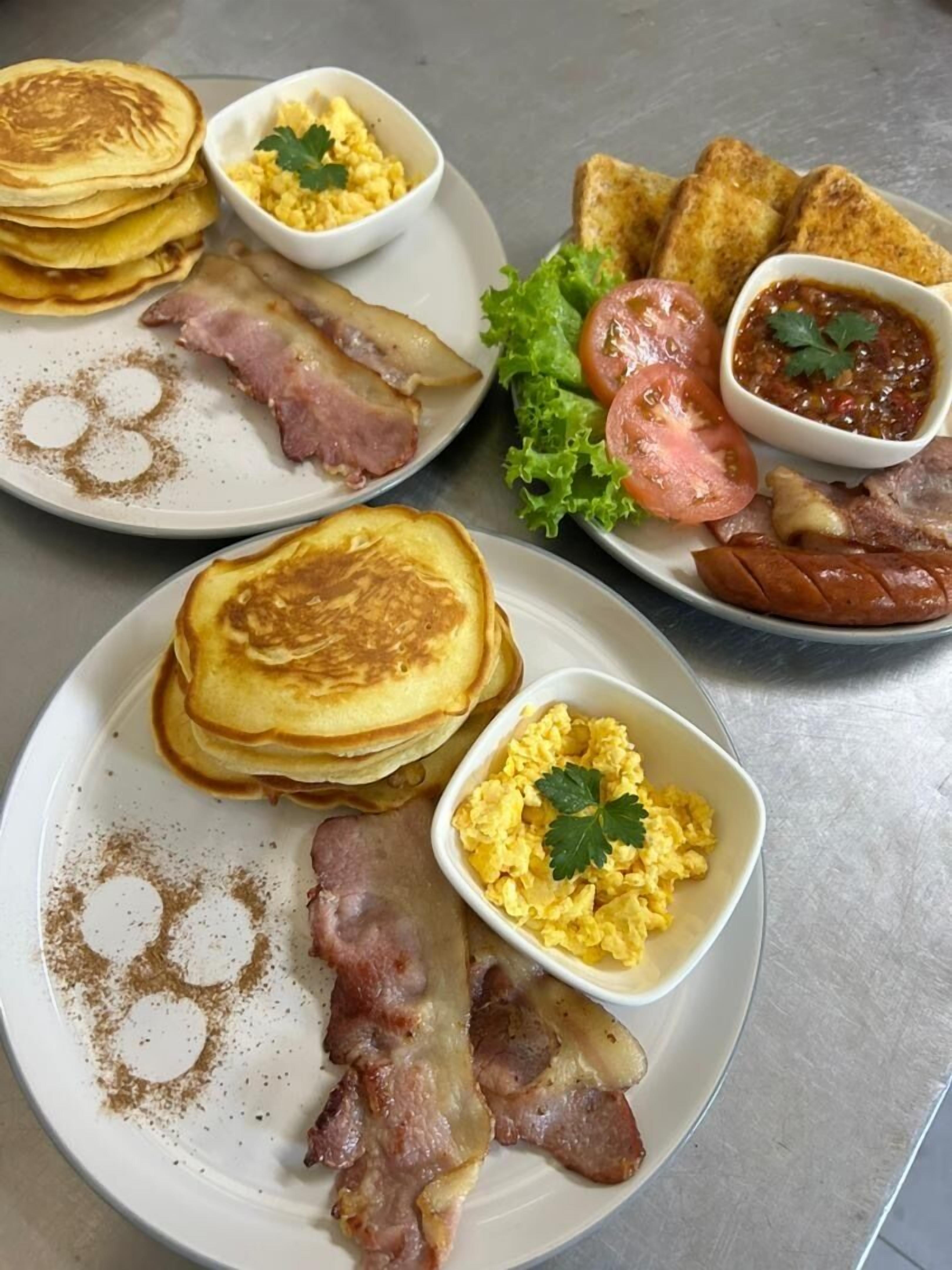A breakfast plate with pancakes, bacon, scrambled eggs, toast, tomatoes, lettuce, and a side of jam.