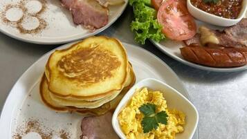 A breakfast plate with pancakes, bacon, scrambled eggs, toast, tomatoes, lettuce, and a side of jam.