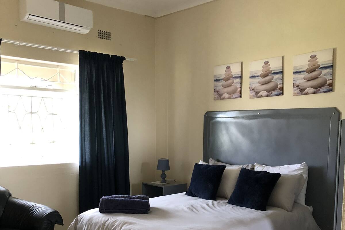 A bedroom with a bed, a nightstand, a lamp, a chair, and a window with curtains.