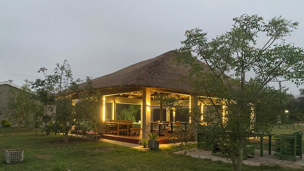 A thatched-roof pavilion with outdoor seating, surrounded by a well-maintained lawn and trees. - Wanakah Estate Guesthouse (Mpaka)