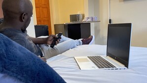 A person sitting on a bed with a laptop and a remote control. - Wanakah Estate Guesthouse (Mpaka)