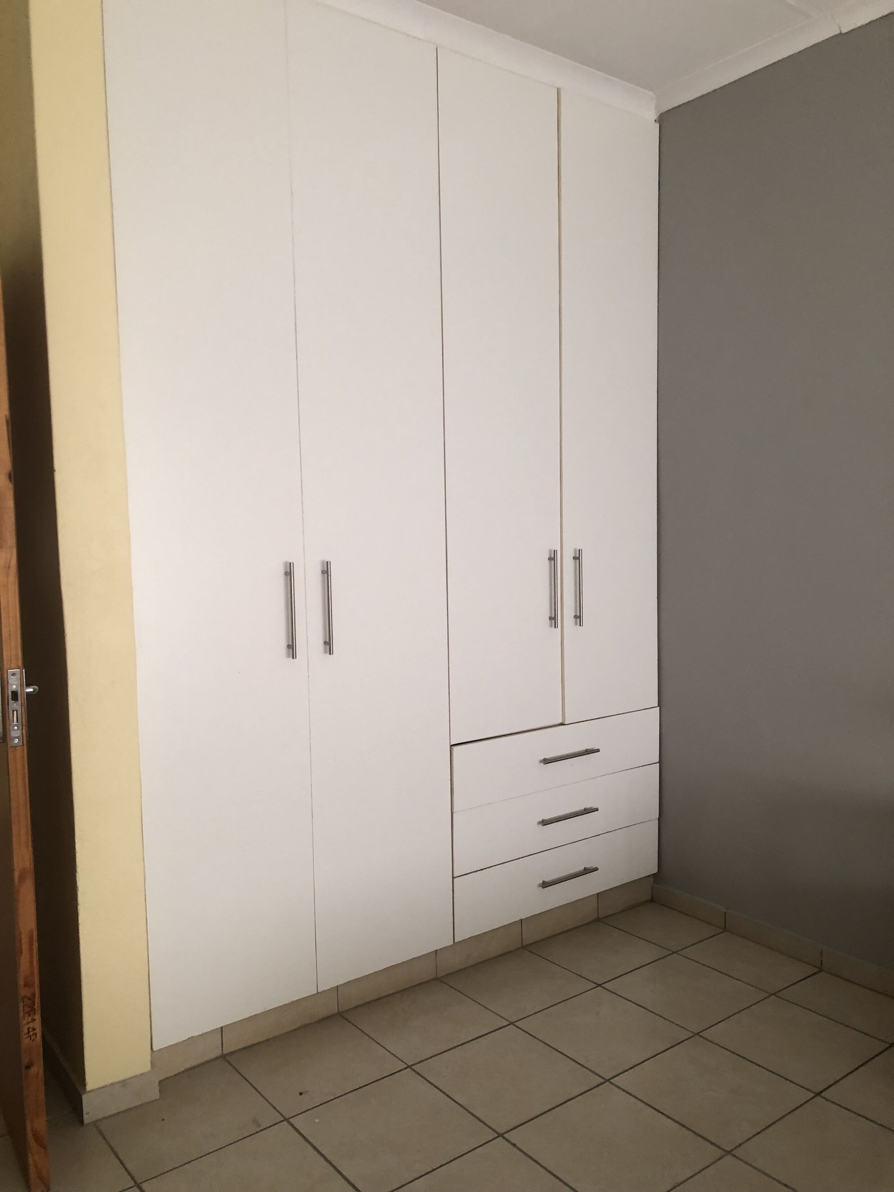 A room with a large white wardrobe, a grey wall, and tiled flooring.