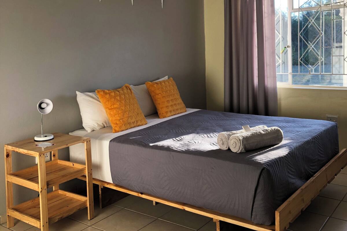 A bedroom with a bed, bedside table, and a window with curtains.