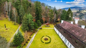 A traditional building with a symmetrical facade, a central circular lawn feature, and a surrounding forested area. - Soví dom flat 2 (Svätý Anton)