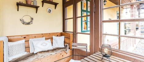 Un banc en bois avec des coussins, une petite table avec une chaise et une fenêtre donnant sur l’extérieur.