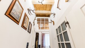 A narrow hallway with wooden beams, framed pictures on the walls, and antlers mounted on the ceiling. - Soví dom flat 2 (Svätý Anton)