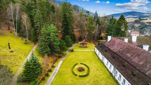 A traditional building with a symmetrical facade, a central circular lawn feature, and a surrounding forested area.