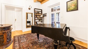 A grand piano in a spacious room with a patterned rug, a bookshelf, and a painting on the wall.