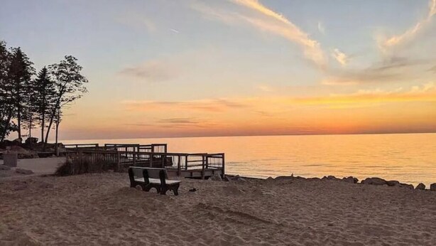 Ein Strand mit einer Holzterrasse und Bänken, mit Blick auf den Ozean bei Sonnenuntergang.