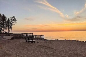 Uma praia com um deque de madeira e bancos, com vista para o oceano ao pôr do sol.